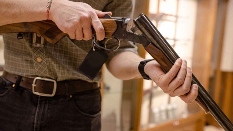 Gun store employee handling a shotgun with a price tag in a firearms retail store
